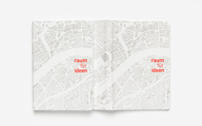 Gefaltetes Notizbuch mit Graustufen-Stadtkarte und rotem Text 'raum für ideen'