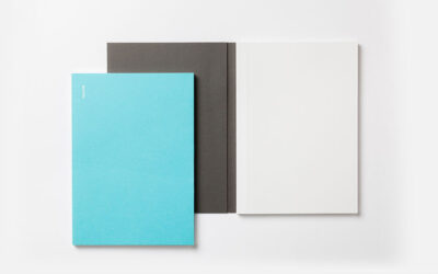 Three notebooks laid on top of each other in the colors turquoise, dark grey, and white