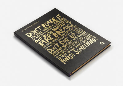 Carnet noir avec une écriture dorée affichant des citations motivantes comme 'Don't force it', 'Take breaks' et 'Finish something'