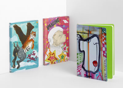Drei bunt illustrierte Notizbücher mit Fantasiemotiven, darunter ein fliegender Adler mit einem Tiger, ein Hunde-Astronaut umgeben von Sternen und ein abstraktes Gesichtskunstwerk