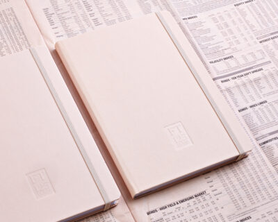 Zwei geschlossene Notizbücher mit geprägtem Siegel auf dem Cover, auf einer Zeitung mit Finanzmarktinformationen