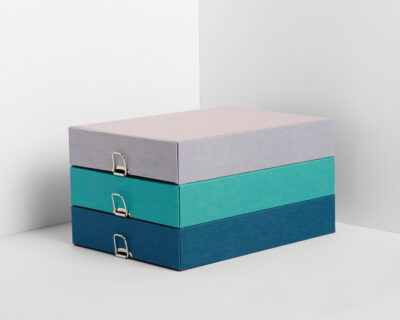 Three stacked archive boxes in a color gradient from light pink to turquoise to dark blue with silver closures