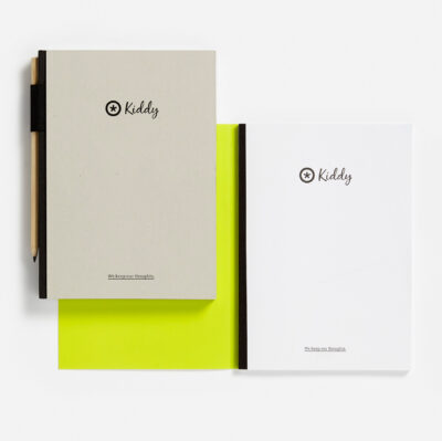Zwei Notizbücher von 'Kiddy' mit minimalistischem Design, eines in Beige und das andere in Weiß, beide mit dem Markenlogo und dem Slogan 'We keep our thoughts'