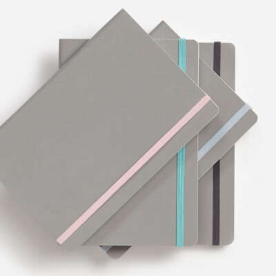Stapel von grauen Notizbüchern mit farbigen Gummibändern in Rosa, Blau und Lila