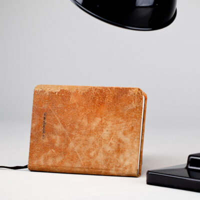 Vintage red-brown leather notebook with 'brandbook' embossing, placed next to a modern black desk lamp