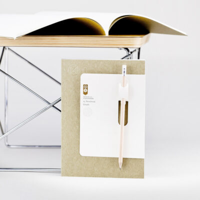 Notebook with a beige-colored pen in a holder in front of an open book on a metal stand