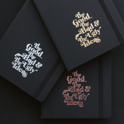 Drei schwarze Notizbücher mit goldener, silbener und bronzener Prägung des Textes 'The Good The Bad & The Ugly Ideas' auf dunklem Hintergrund
