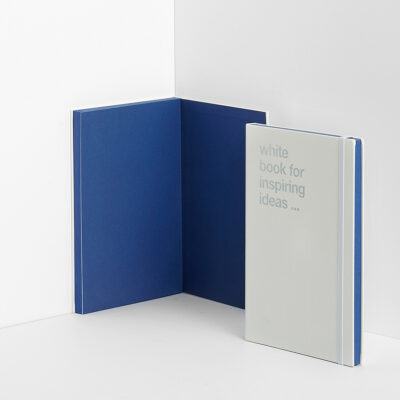 Offenes blaues Notizbuch und geschlossenes weißes Notizbuch mit Aufschrift 'white book for inspiring ideas'