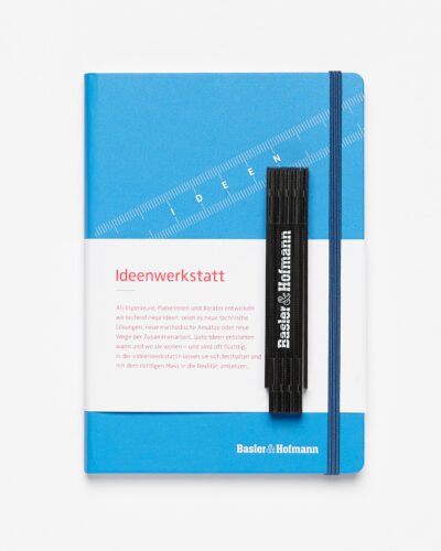 Carnet bleu intitulé 'Ideenwerkstatt' et un passage descriptif, accompagné d'une règle noire avec le branding 'Basler & Hofmann'
