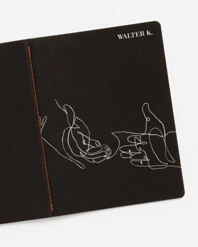 Schwarzes Notizbuch mit weißer Linienzeichnung von Händen und der Aufschrift 'WALTER K.' auf dem Cover, mit orange-roter Fadenbindung an der Seite